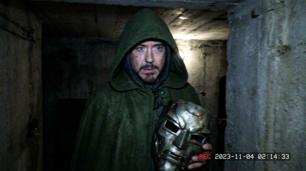 Robert Downey Jr as Doctor Doom holding a Doctor Doom mask in a dark room.