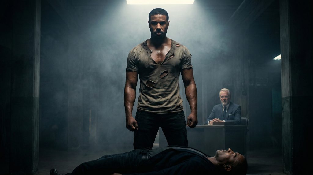 Cinematic wide still from Sinners featuring a hyper-shredded Michael B. Jordan in a smoky factory setting, captured with dramatic lighting.
